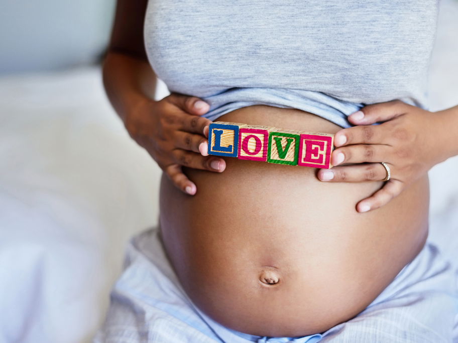 Eine Mama hält ein Love-Schild über ihren kugelrunden Babybauch.