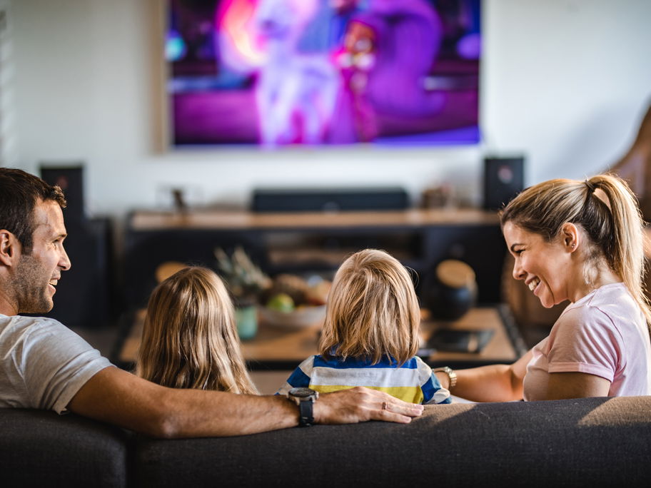 Mutter und Vater sitzen mit Sohn und Tochter auf dem Sofa vor dem Fernseher.