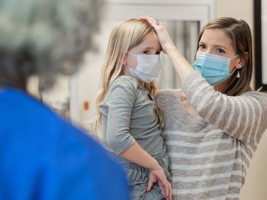 Mutter mit ihrer kranken Tochter am Empfang einer Kinderarztpraxis