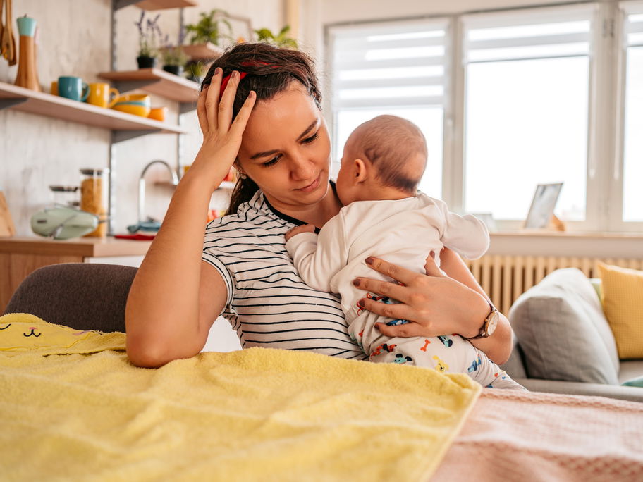 Junge Mutter mit Baby auf dem Arm fasst sich an den Kopf