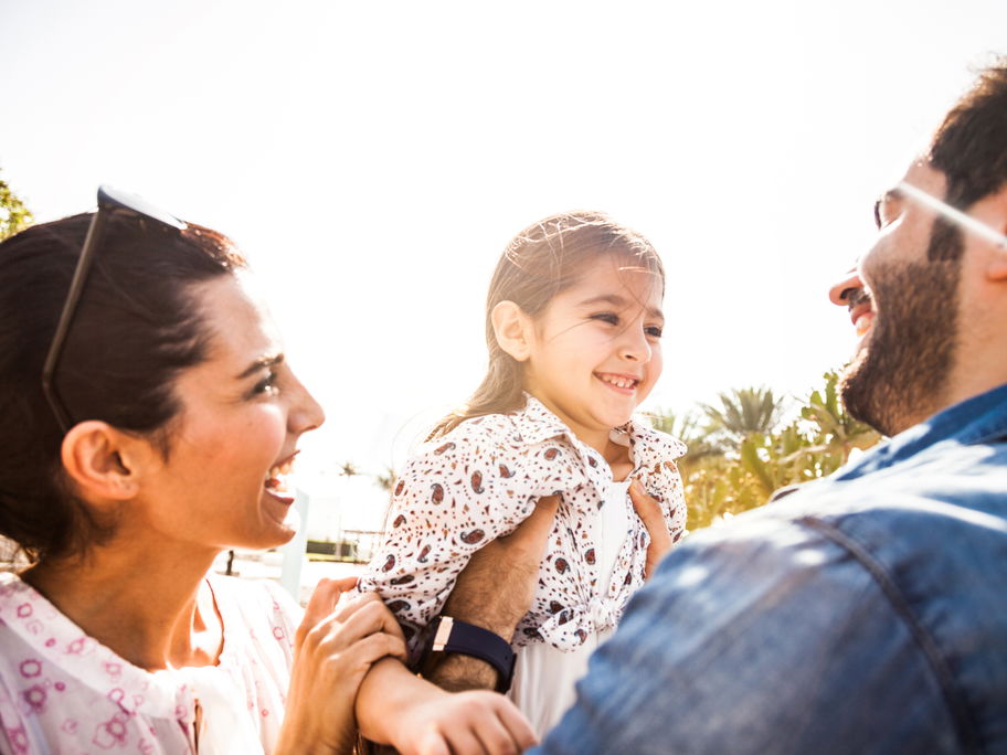 Mutter und Vater halten ihre lachende Tochter.