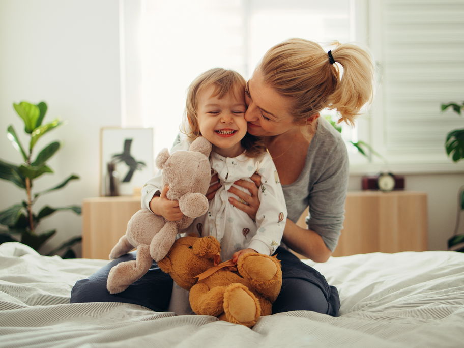Mama umarmt Mädchen mit Kuscheltieren
