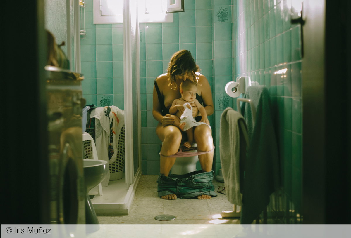 Eine Mutter sitzt übermüdet auf der Toilette mit ihrem Baby auf dem Schoß