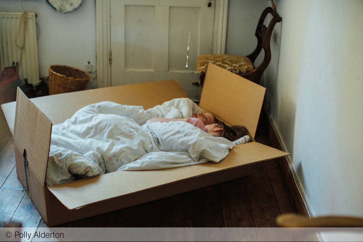 Zwei Kinder kuscheln sich in ein selbstgebautes Bett in einem Karton