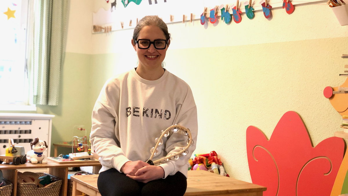 Eine Erzieherin sitzt mit einer Rassel in der Hand in einer leeren Kita