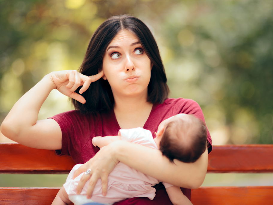 Mutter mit Baby im Arm hält sich die Ohren zu.
