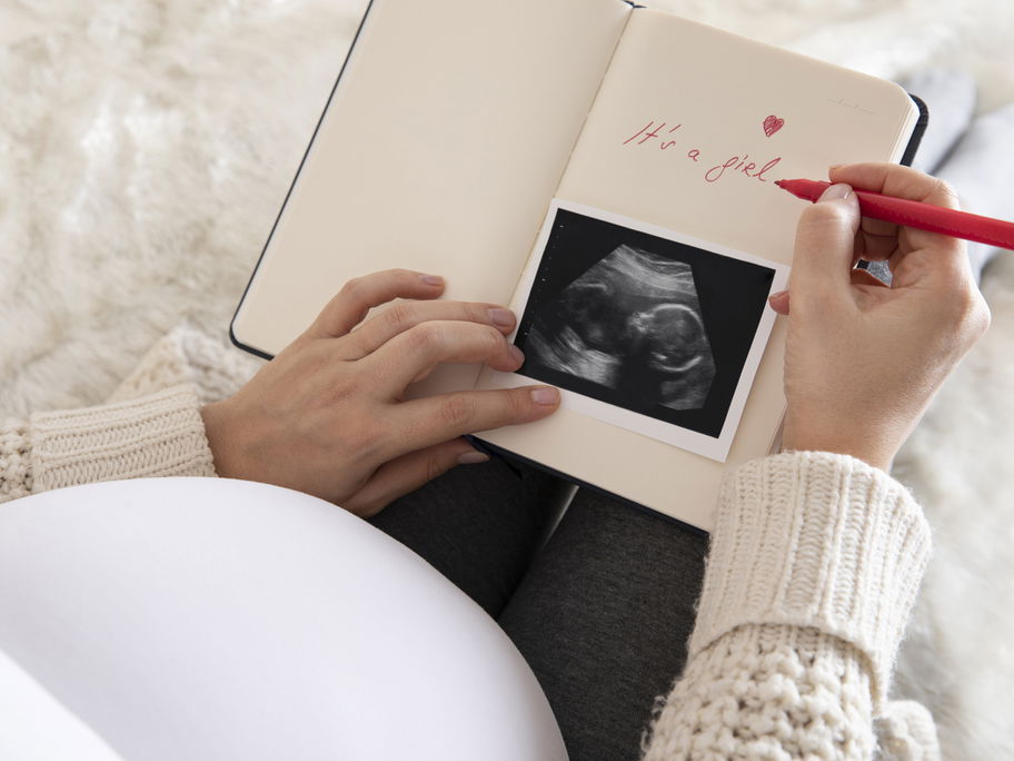Eine schwangere Frau schreibt in ihr Baby-Tagebuch und zeigt ihr Ultraschallbild.