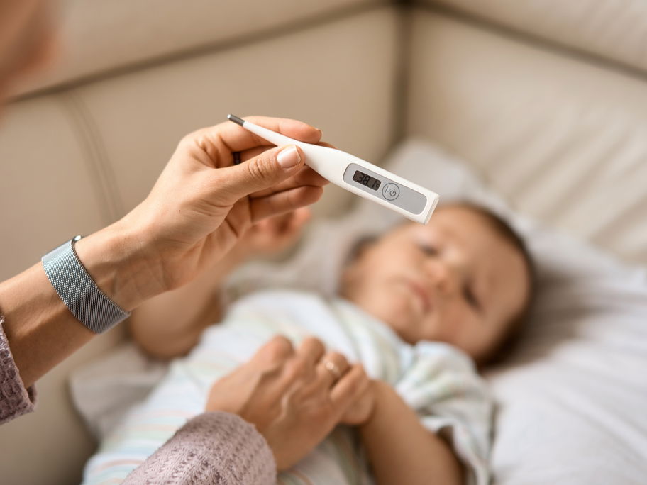 Eine Mutter hält das Fieberthermometer über ihrem Baby.