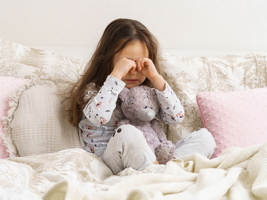 Mädchen sitzt im Schlafanzug auf dem Bett und weint