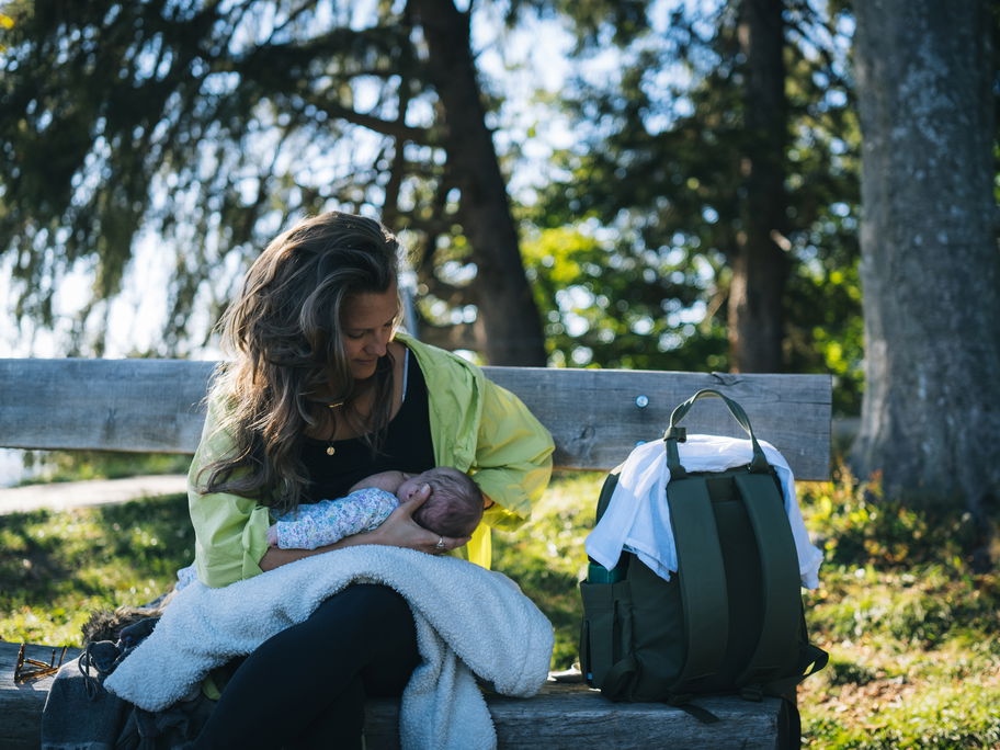 Eine Frau, die ihr Baby auf einer Bank im Grünen stillt.