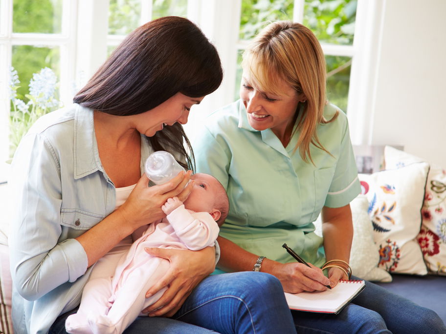 Mutter füttert ihr Baby, Mütterpflegerin sitzt daneben