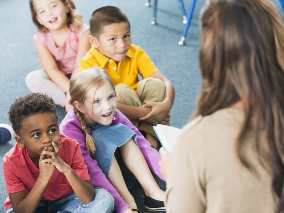 Kindergartenkinder hören einer Erzieherin beim Vorlesen zu