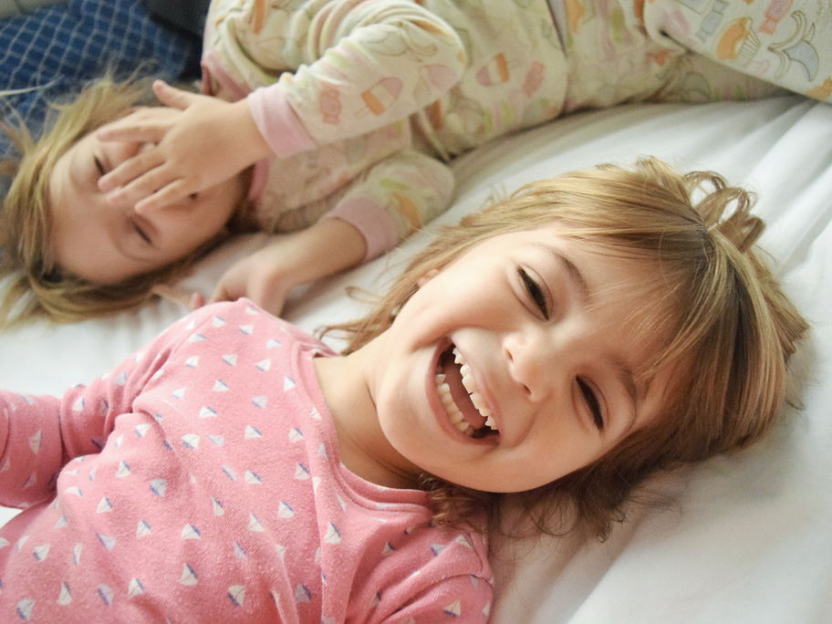 Zwei Kinder liegen lachend im Bett