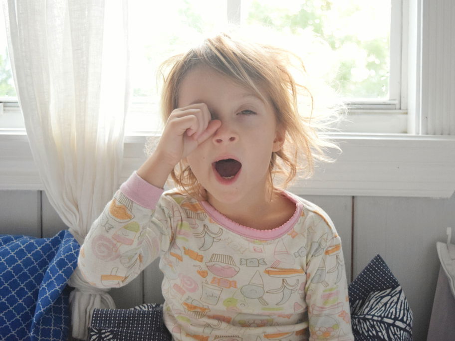 Blondes Mädchen reibt sich am Morgen die Augen und gähnt