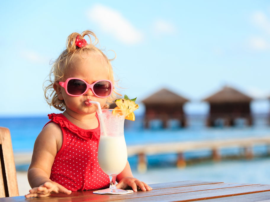 Ein kleines Mädchen mit rotem Badeanzug und Sonnenbrille trinkt einen Kinder-Cocktail.