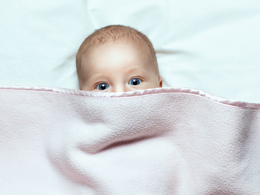 Baby versteckt sich unter einer Decke.