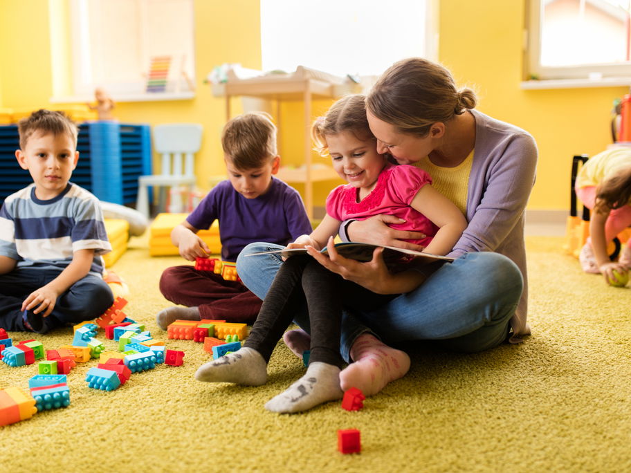 Erzieherin liest einem Vorschulmädchen ein Buch vor und beide lächeln