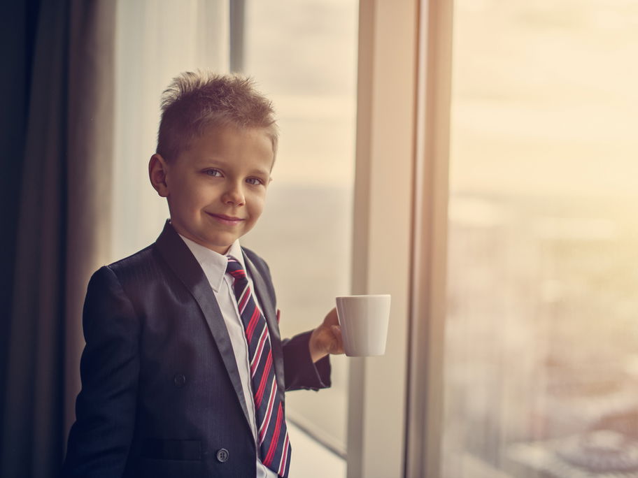 Ein Junge steht im Anzug am Fenster mit einer Kaffeetasse.