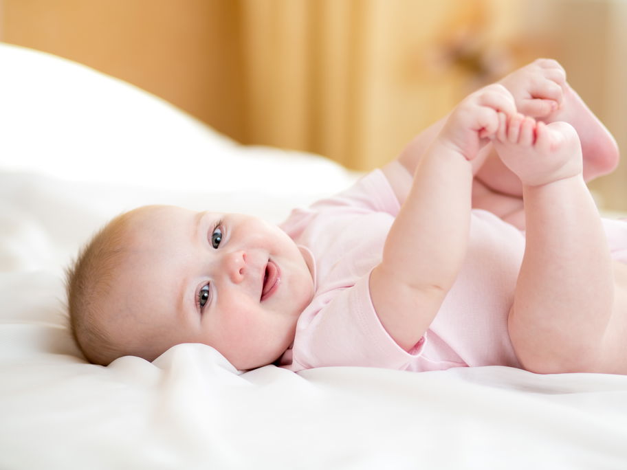 Ein kleines Baby liegt auf dem Rücken und hält sich die Füße.