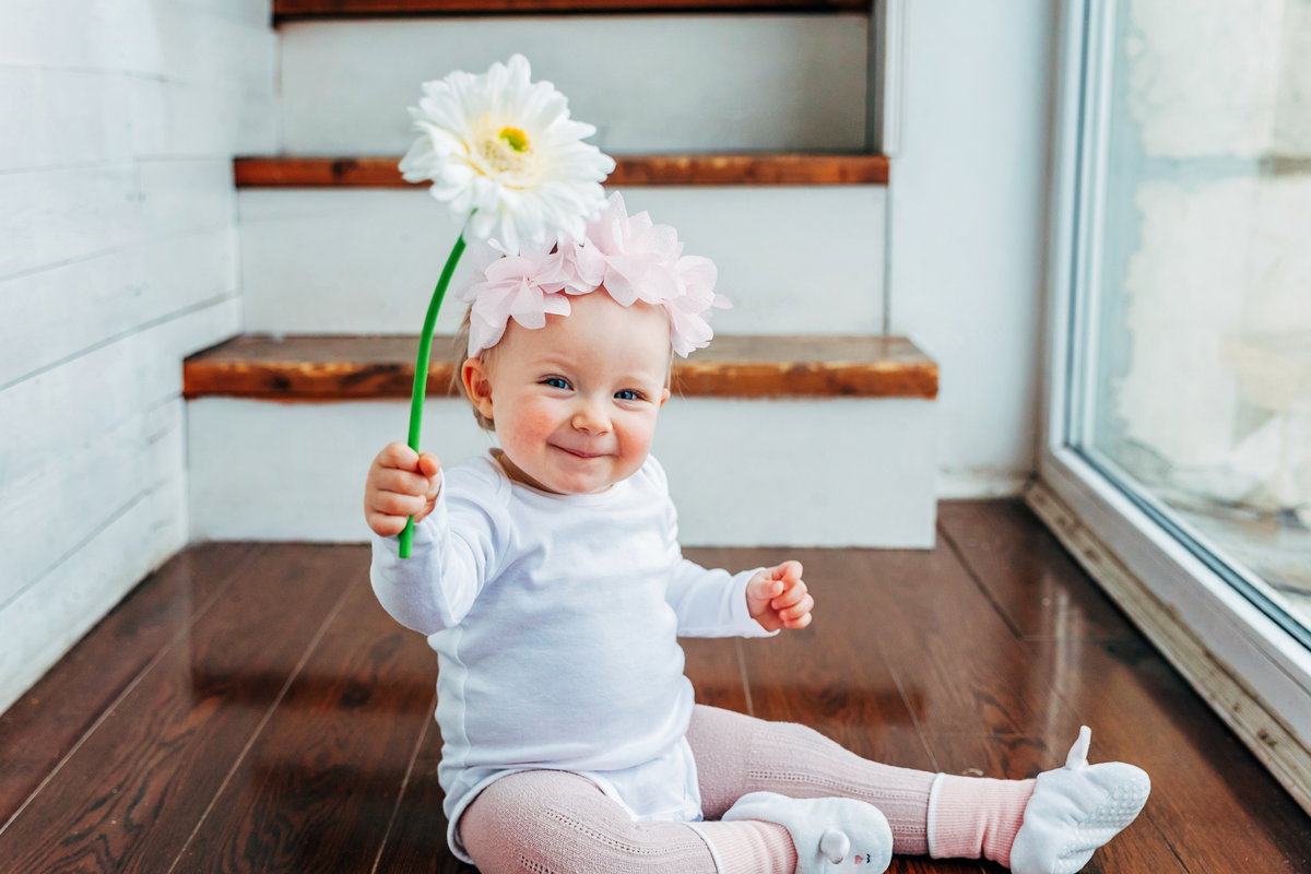 Ein kleines Mädchen lacht und hält eine Blume in der Hand.