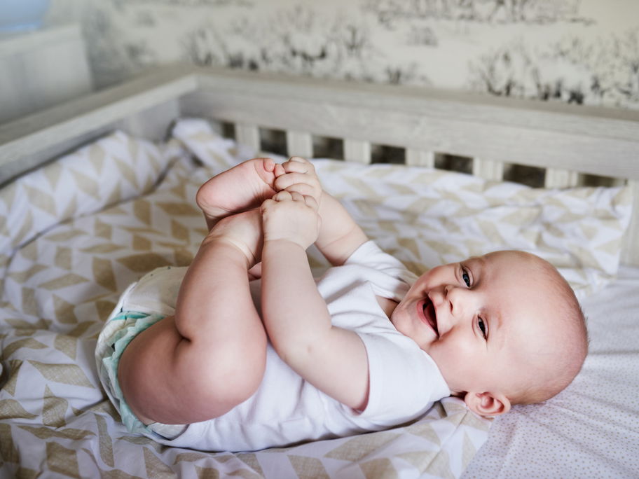Ein Baby liegt in seinem Bett und hält sich die Füße.