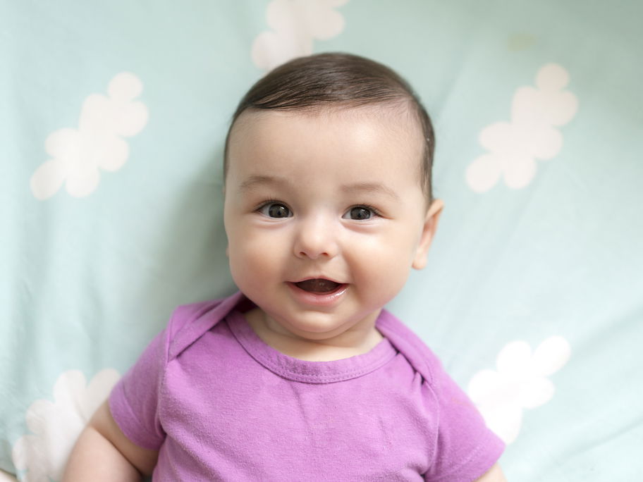 Ein Baby liegt lächelnd auf einer Decke mit kleinen Wolken.