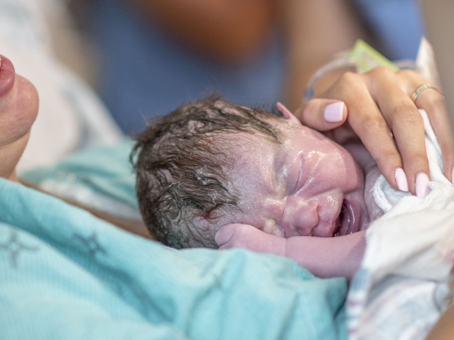 Ein neugeborenes Baby liegt auf dem Bauch seiner Mutter.