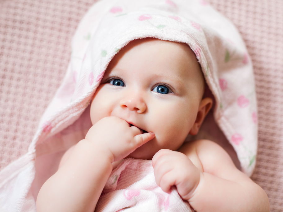 Ein kleines Baby liegt in rosa Bademantel auf einem Tuch.