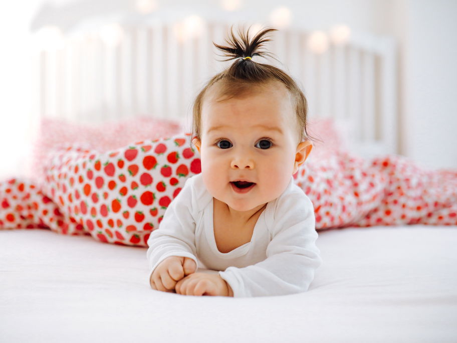 Ein Baby liegt lächelnd auf dem Bett.