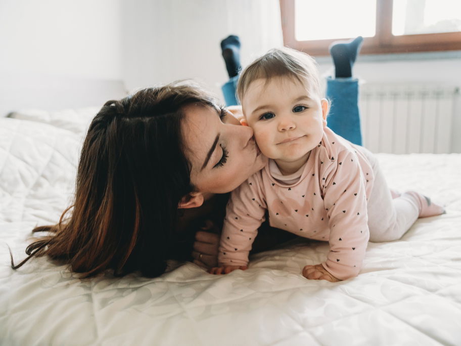 Eine junge Mutter küsst ihre kleine Baby-Tochter auf die Wange.