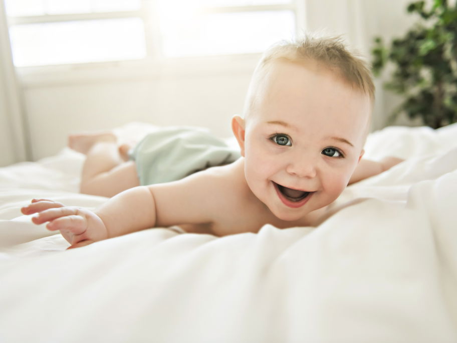 Ein kleiner junge liegt lachend auf dem Bett.