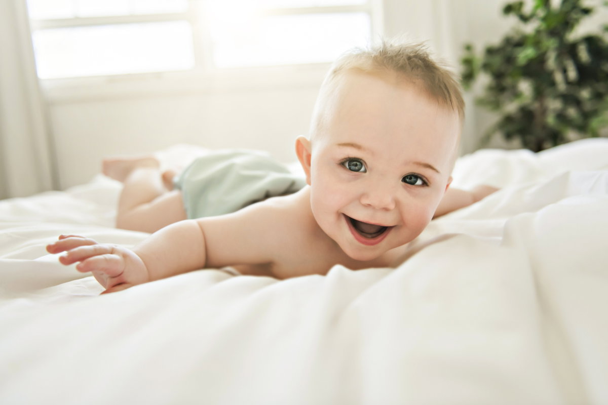 Ein kleiner junge liegt lachend auf dem Bett.