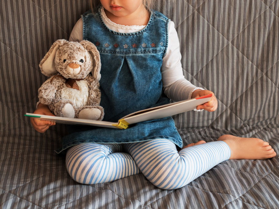 Mädchen liest zusammen mit Kuscheltier ein Kinderbuch