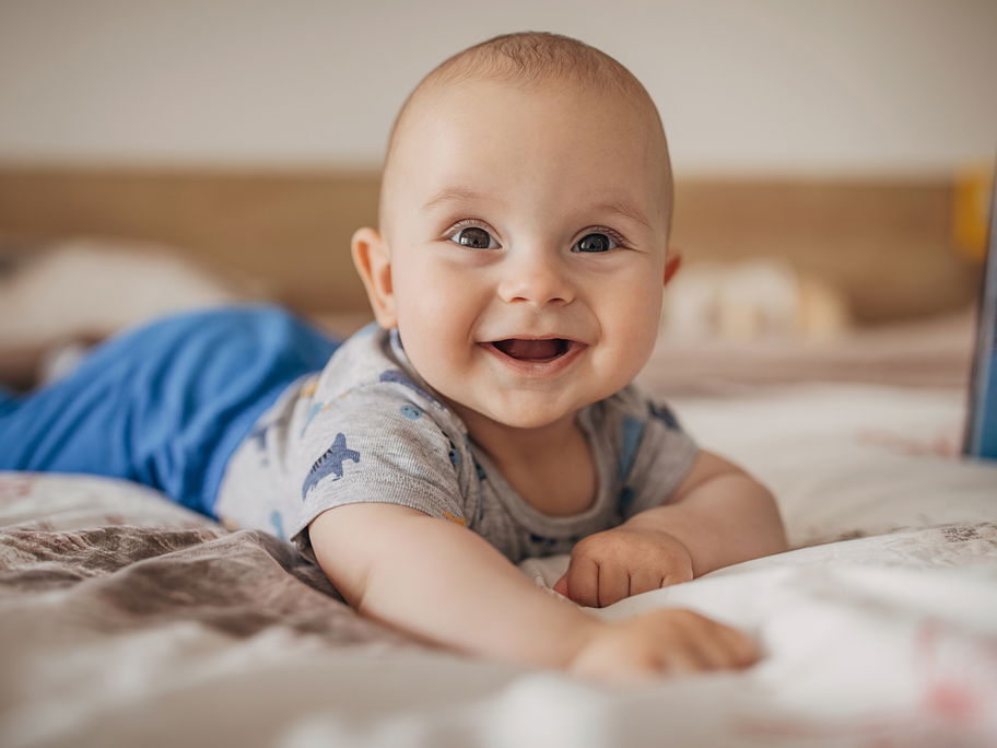 Ein Baby liegt lachend auf dem Bauch.