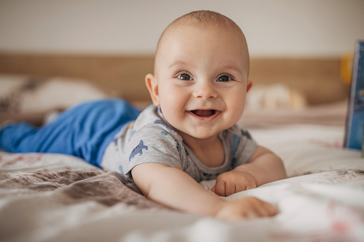 Ein Baby liegt lachend auf dem Bauch.