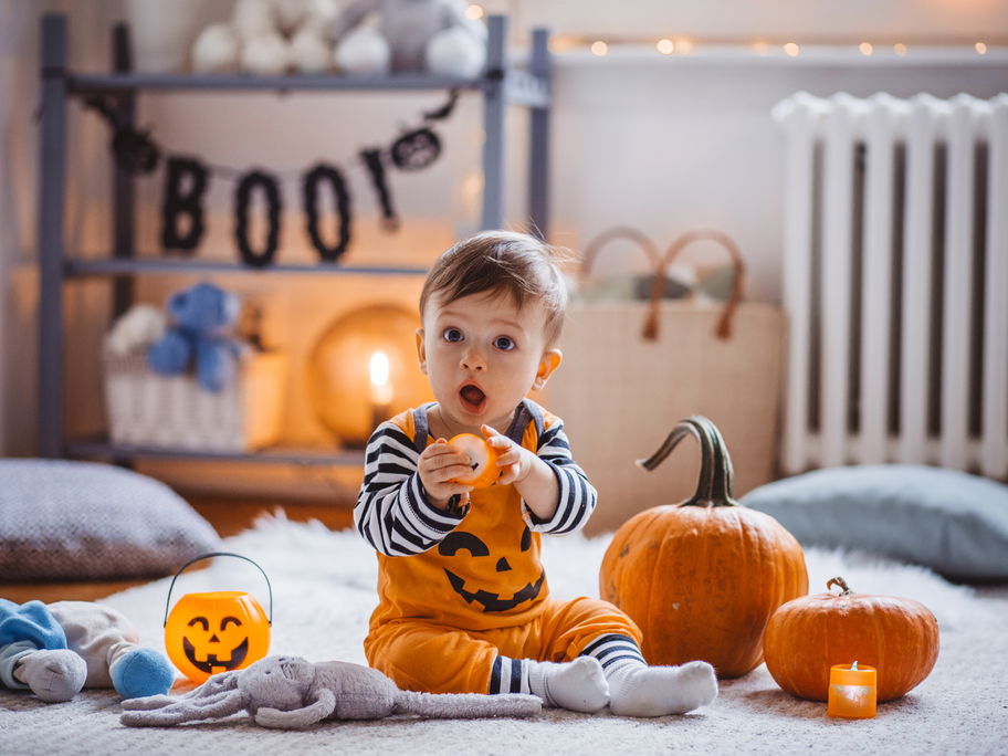 Ein kleiner Junge sitzt als Kürbis verkleidet zwischen Halloween-Dekoration.