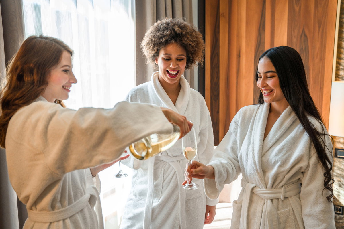 Spa-Day: Drei Freundinnen schenken sich Sekt im Wellness-Bademantel ein