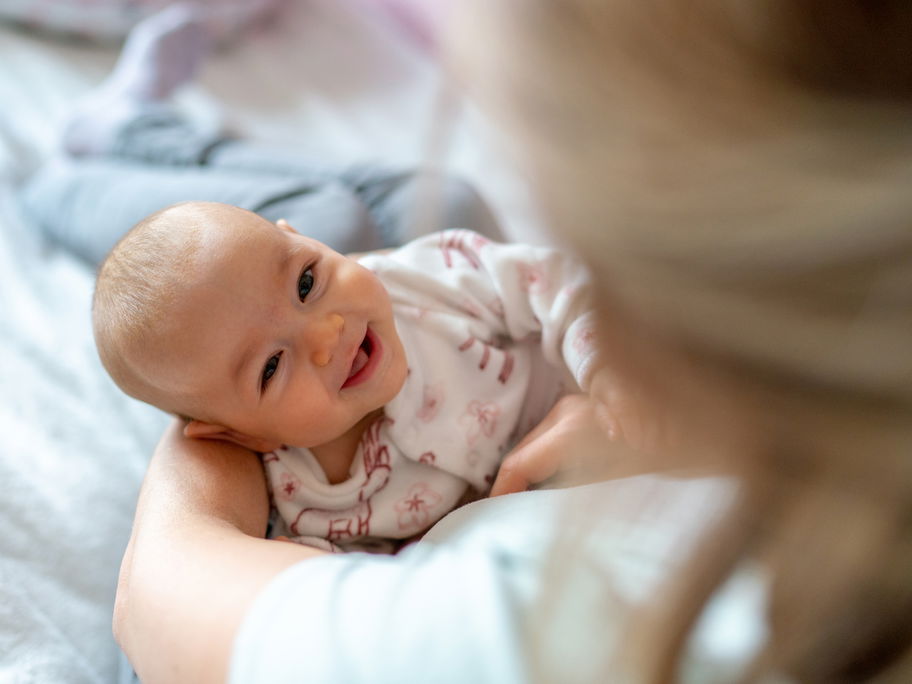 Ein Baby liegt lachend in Mamas Armen.