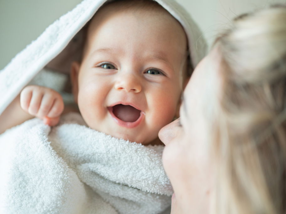 Ein Baby ist in ein Handtuch eingewickelt und lacht.