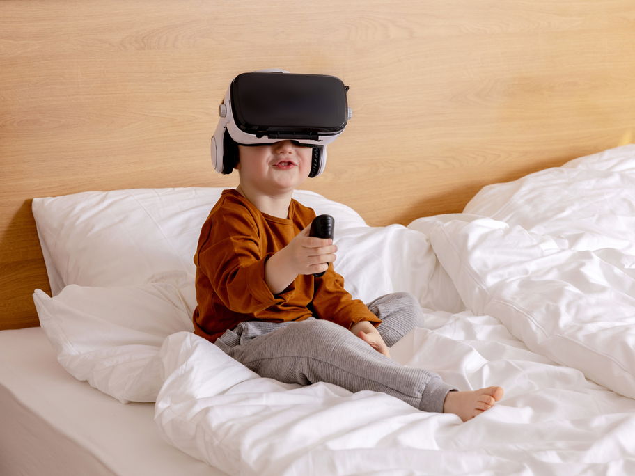Ein kleiner Junge sitzt auf dem Bett und hat eine VR-Brille auf.