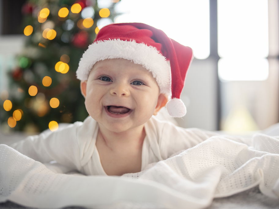 Ein Baby hat eine Weihnachtsmütze auf und lacht.
