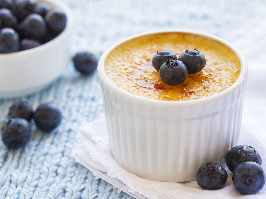 Eine Crème brulée steht auf dem Tisch und ist mit Blaubeeren garniert.