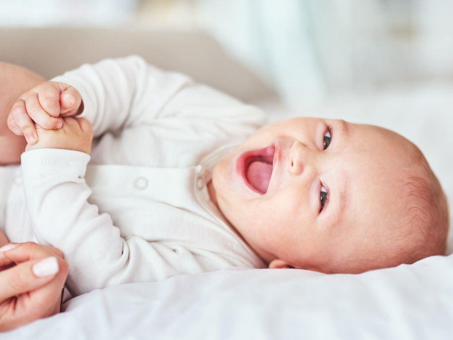 Ein kleines Baby liegt lachend auf dem Bett.