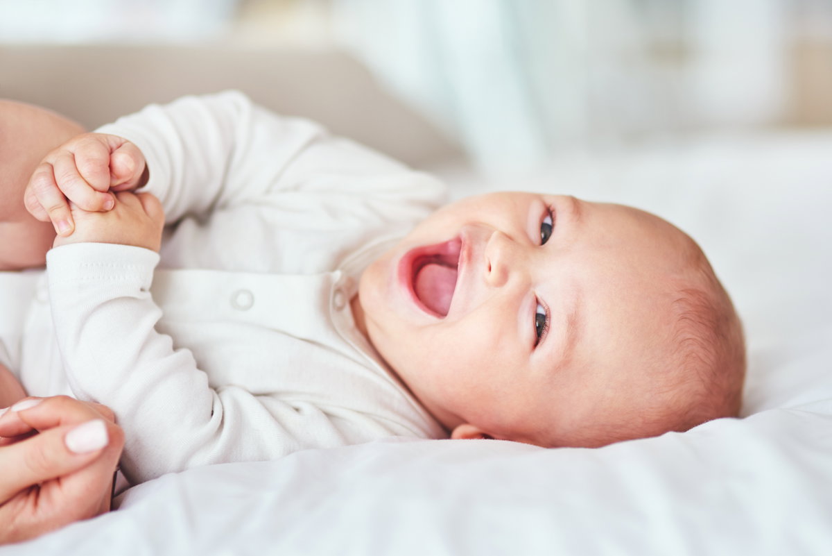 Ein kleines Baby liegt lachend auf dem Bett.