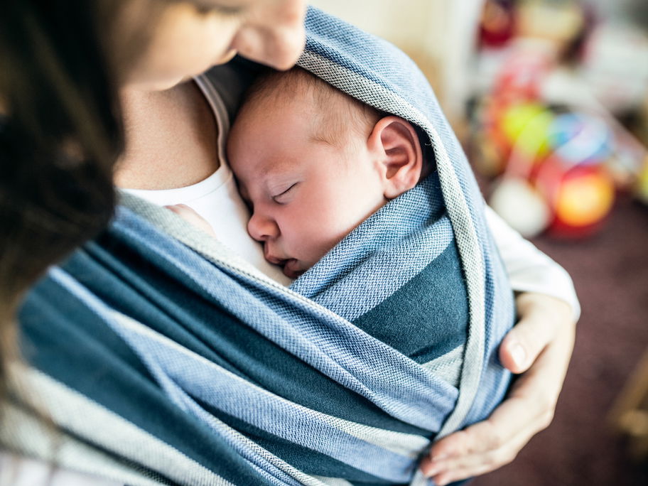 Baby im Tragetuch vor der Brust seiner Mutter.