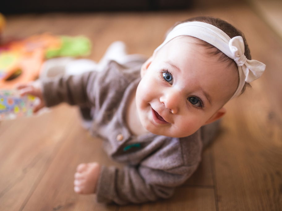 Ein Baby krabbelt neben Spielsachen auf dem Boden.