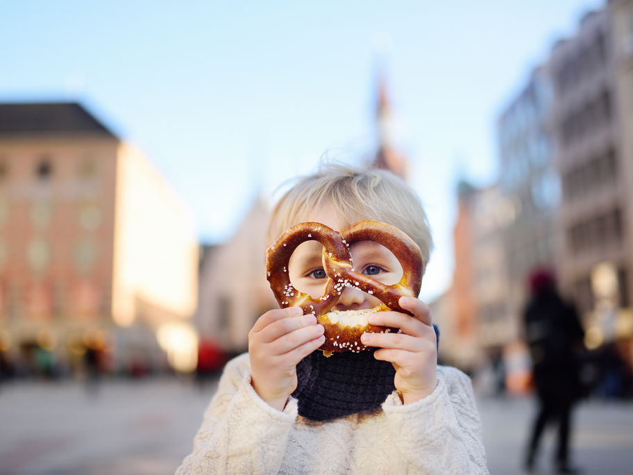 Ein kleiner Junge hält sich eine Brezel vor das Gesicht.