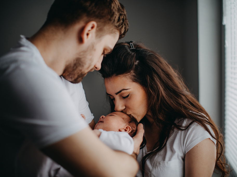 Junge Eltern küssen ihr frischgeborenes Baby.