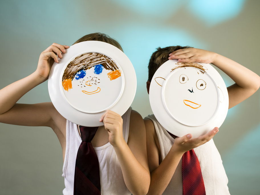 Zwei Jungen halten Teller hoch, auf die ein Gesicht gemalt ist.