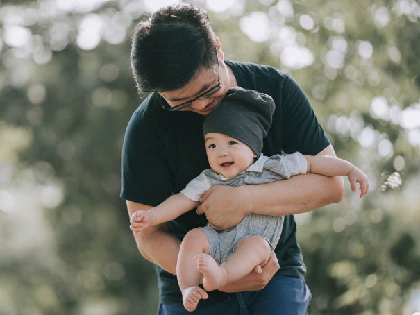 Ein asiatischer Vater trägt seinen Baby-Jungen auf dem Arm.